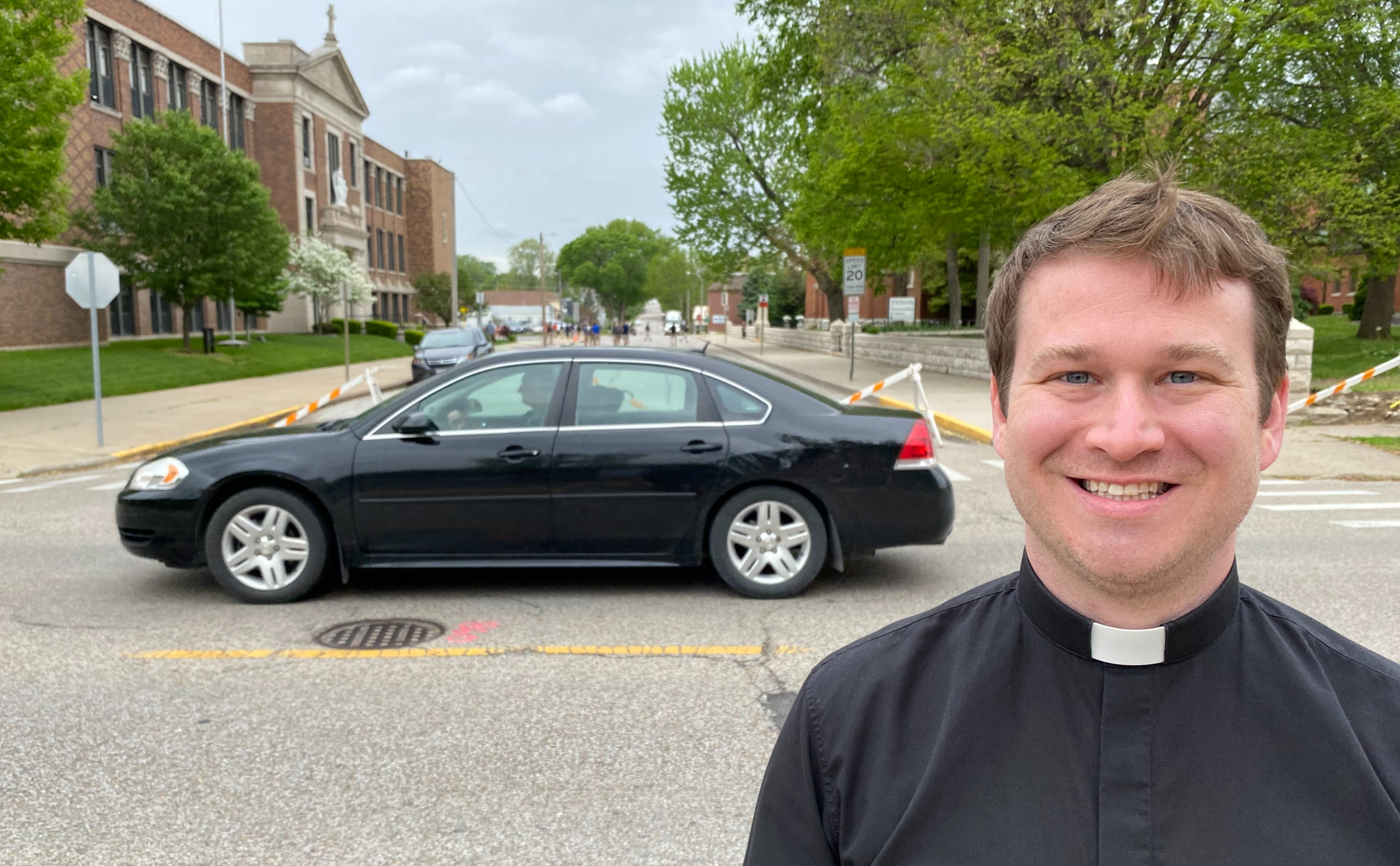 Father Steven Arisman, pastor of St. Francis Solanus Church in Quincy, Ill., stands on the sidewalk on the east side of 18th Street with children playing in the street between St. Francis School and St. Francis Parish.