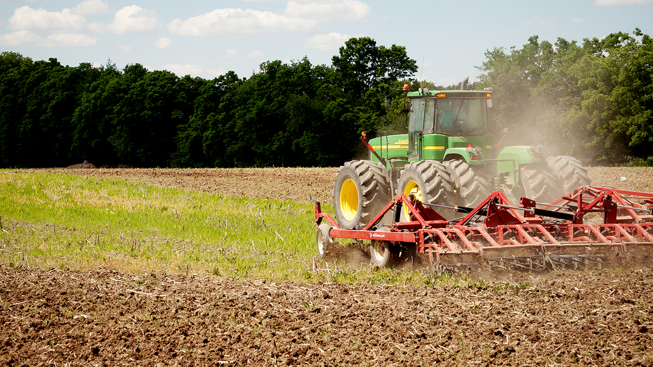 Grabill, Indiana - June 13th, 2011: John Deere green tractor tilling the ground to prepare for summer planting of hay, corn, and soybeans in Indiana, USA. Driving through the field with a disk tiller.