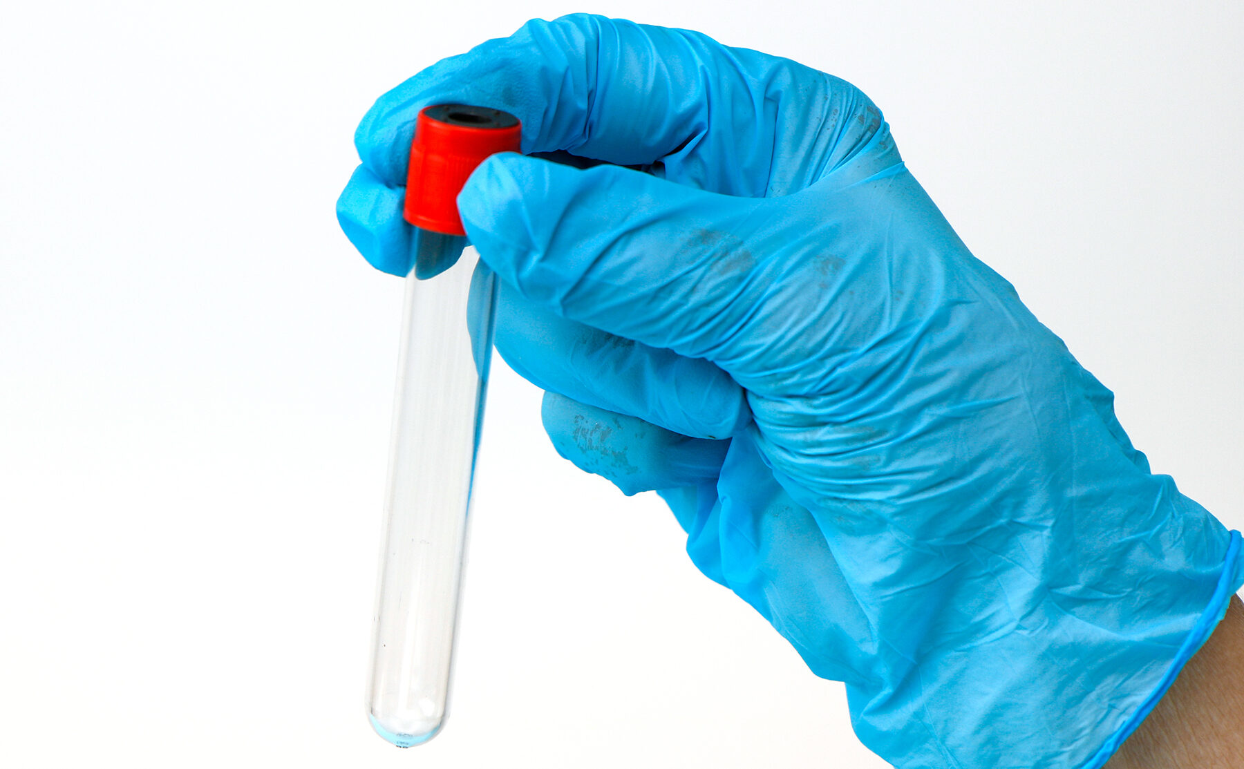 a hand in a medical glove holds an empty test tube on a light background with copy space.