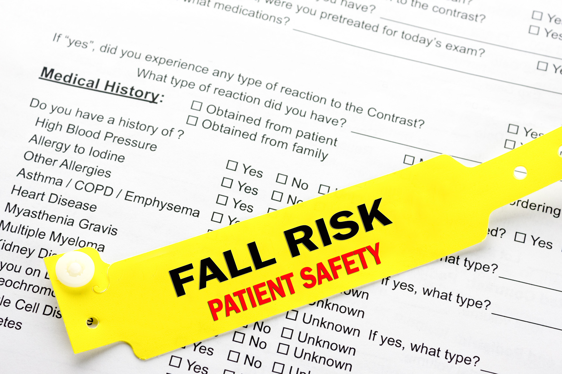 A yellow fall risk patient  safety bracelet on top of a hospital questionnaire paperwork