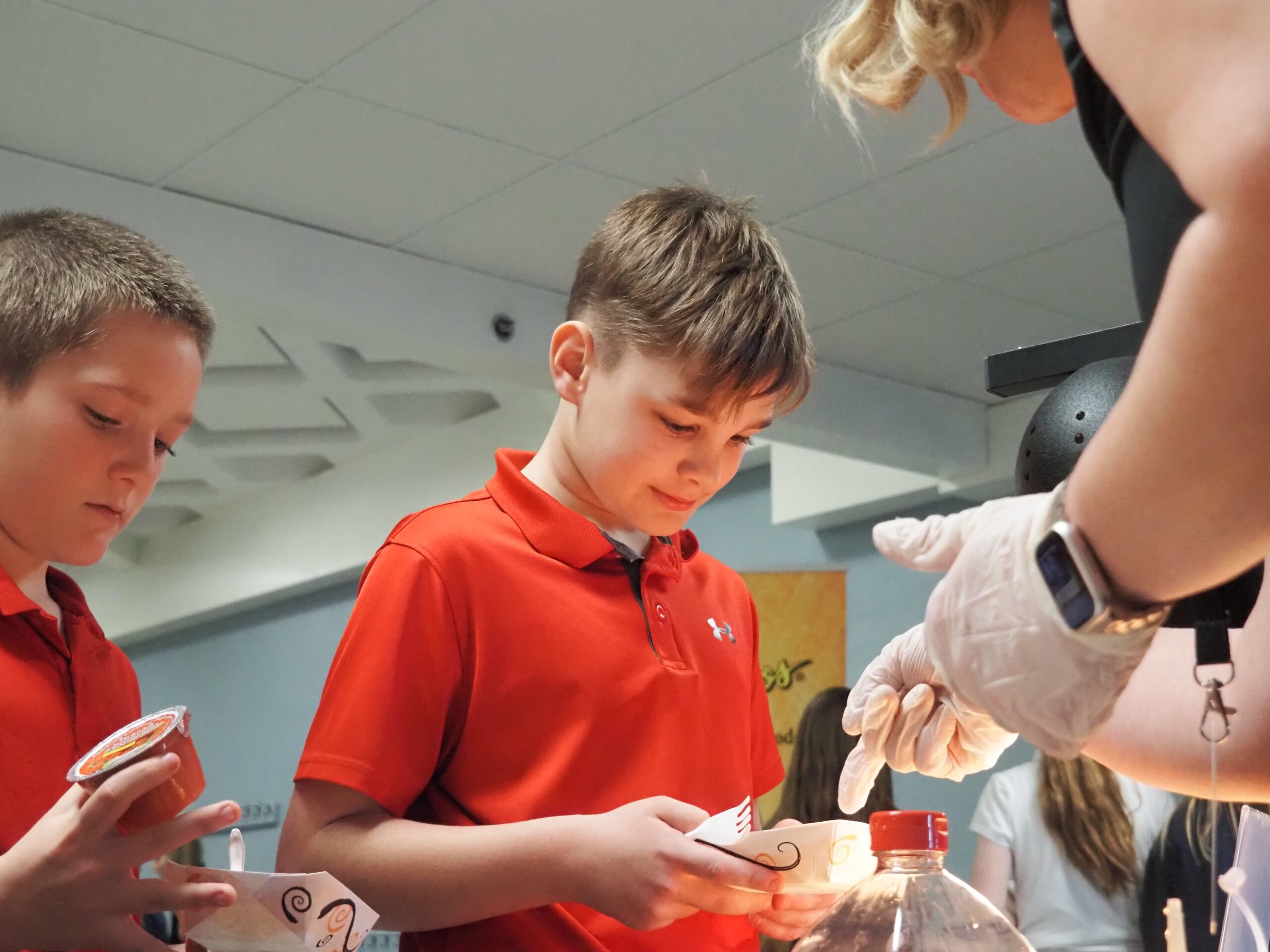 Fourth graders Caleb Holtschlag (left) and Harry Stevens (right) learn more about the hot honey chicken bites on their plates during Try Day, a tasting event hosted by Kohl Wholesale. | Photos by Aspen Gengenbacher