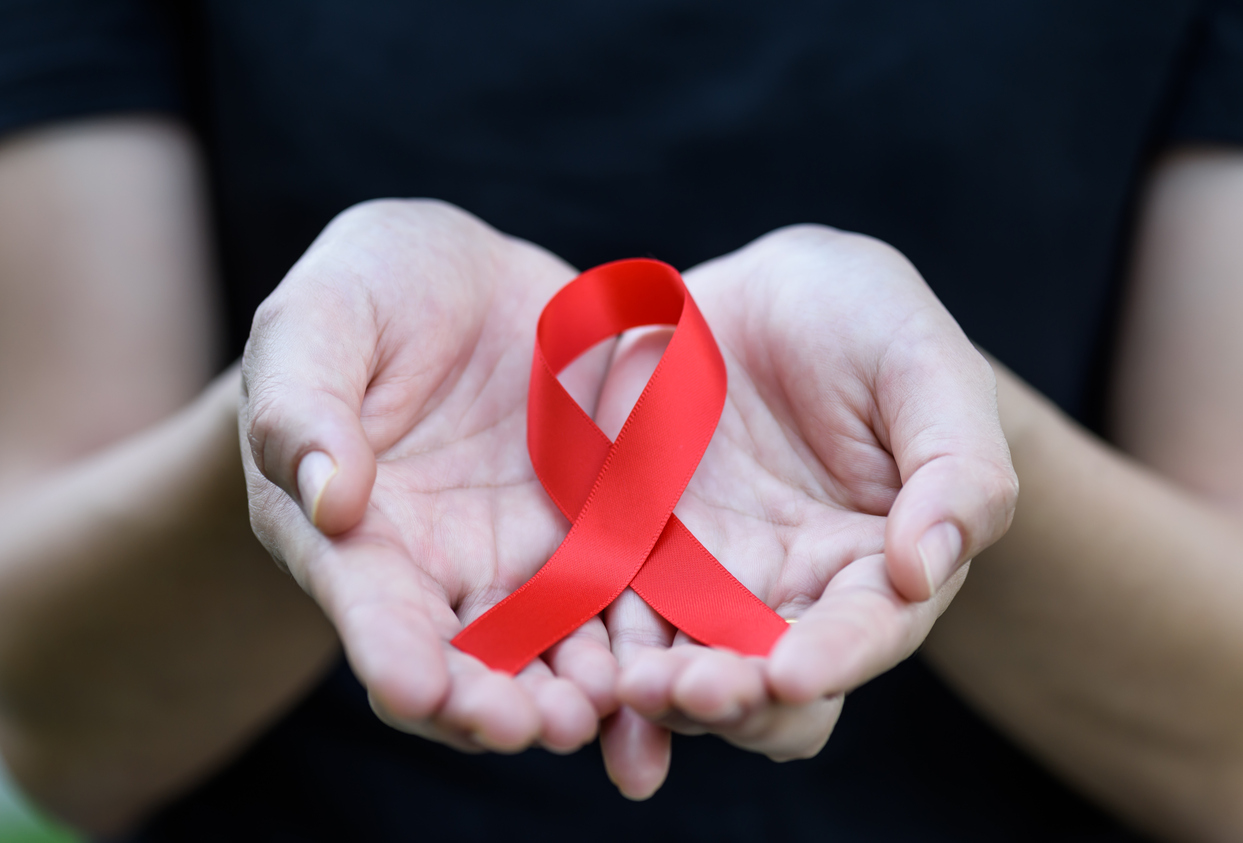 Female hands holding red AIDS awareness ribbon. Aids Awareness campaign. Female hands holding red AIDS awareness ribbon. Aids Awareness campaign.